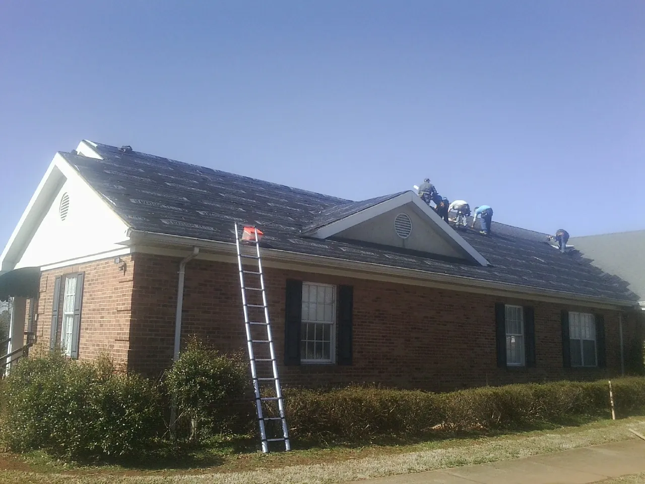 Crew tearing shingles off a brick ranch roof with a ladder set — Emergency Roof Repair work by our crew in Arapahoe