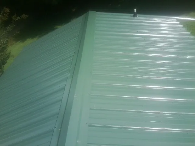 New green metal panels meeting at the ridge of a roof — Flat Roof Repair work by our crew in Arapahoe