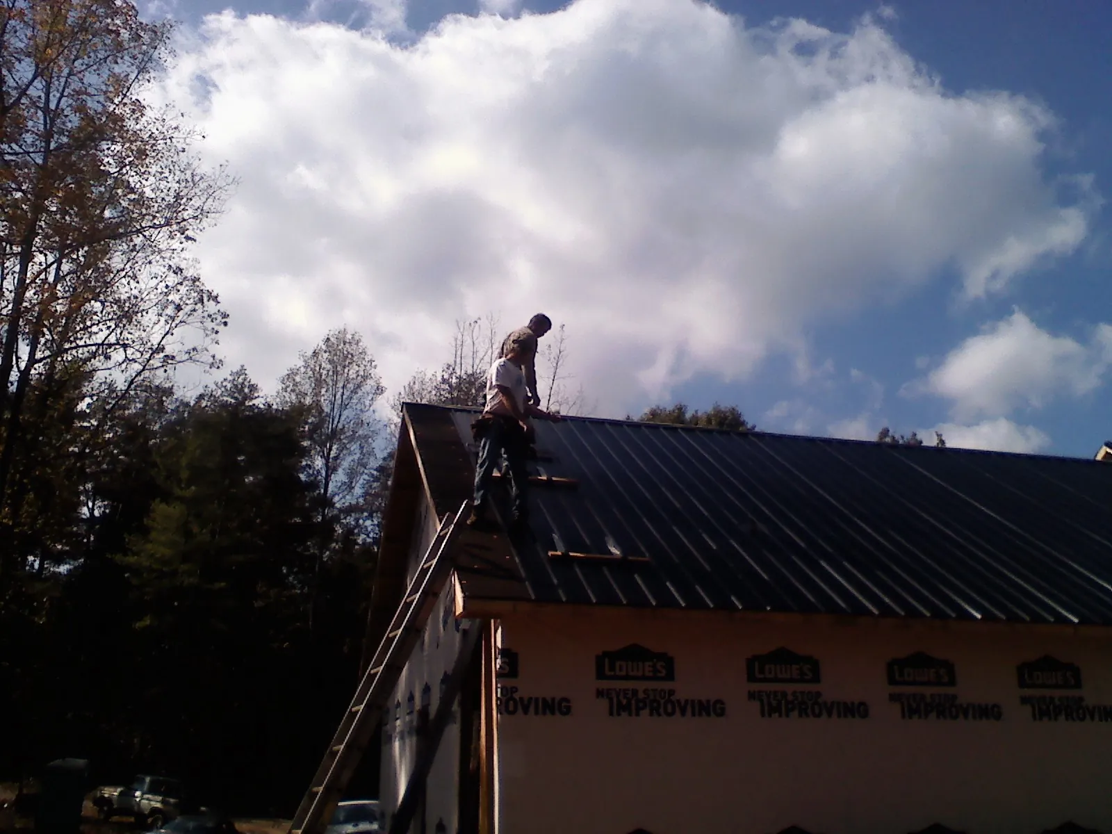 Roofer fastening dark metal panels high against a cloudy sky, from a Roof Inspection job in Arapahoe