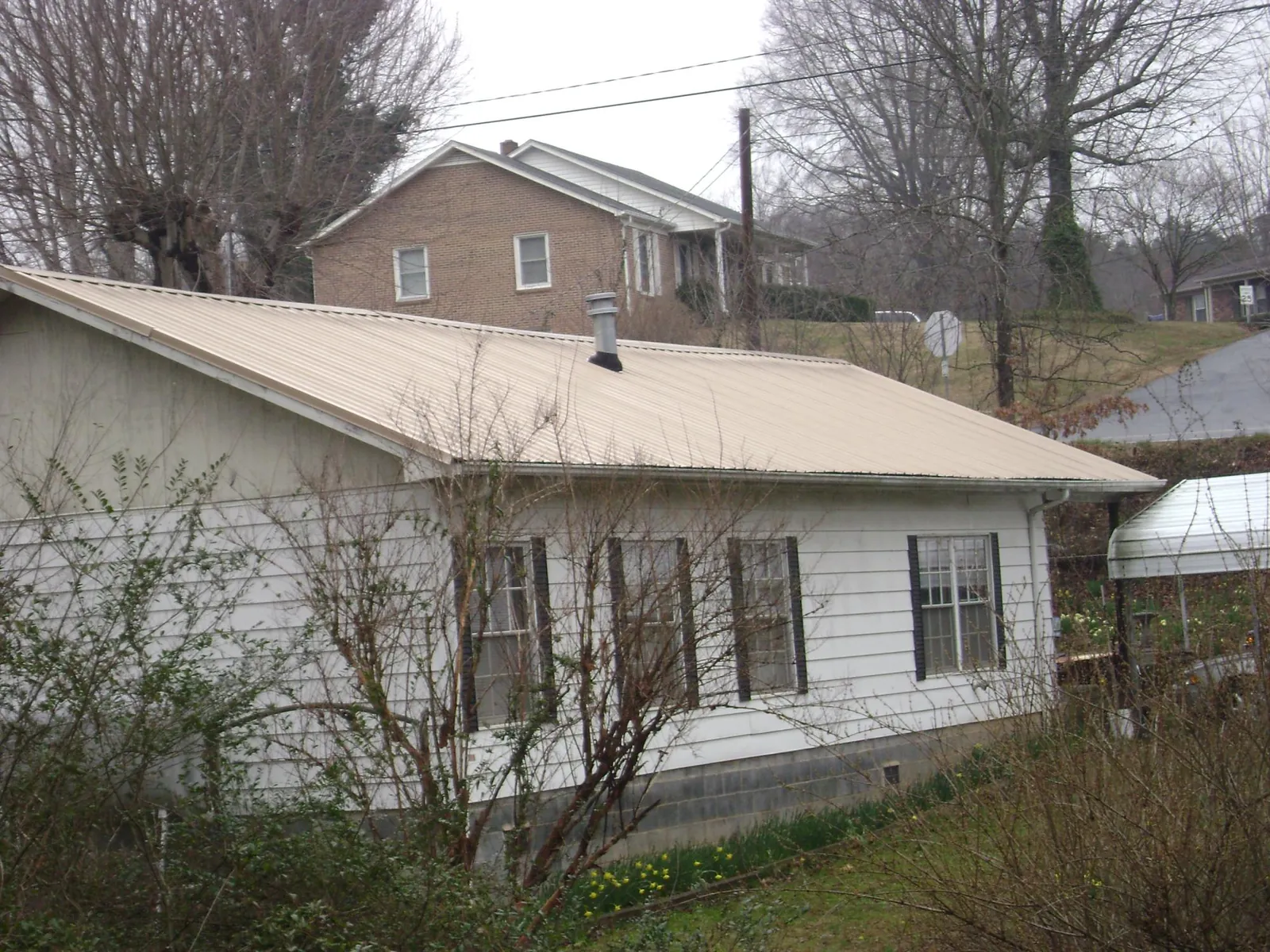 Tan metal roof on a white sided house set into a hillside — Commercial Roofing by Roofing Brothers in Arapahoe