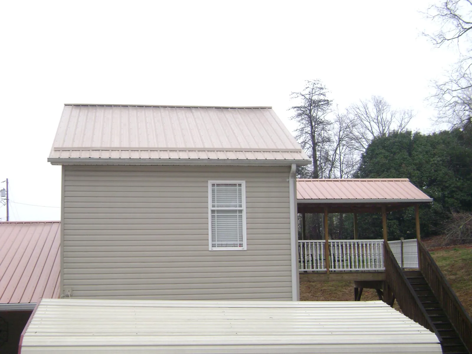Tan metal roofs on a two story addition and attached porch, from a Roof Replacement job in Arapahoe